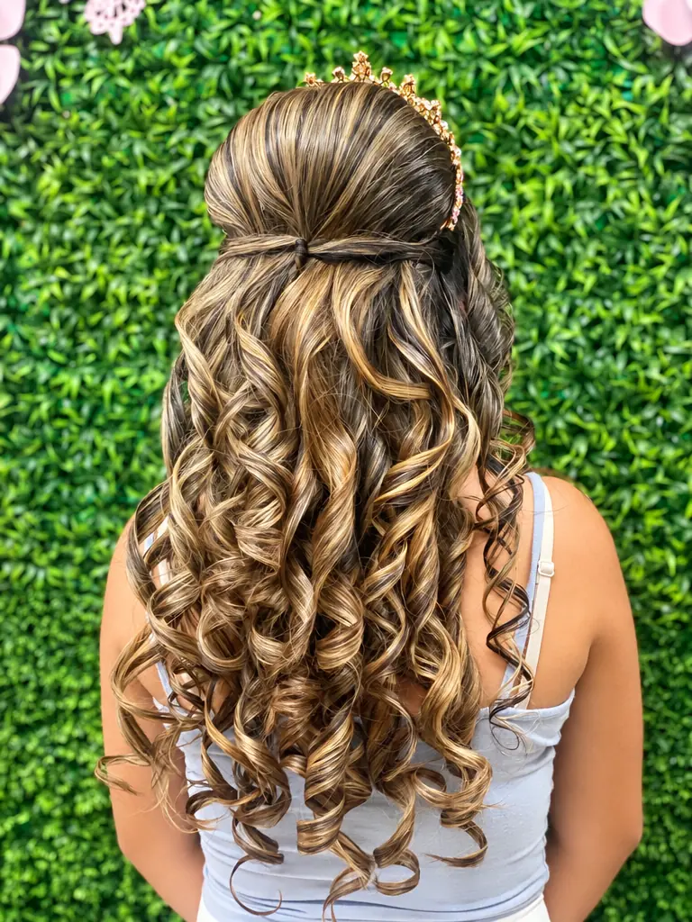 Half-up curls with a tiara in front of a green leaf wall, back view